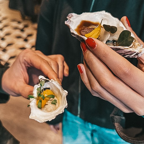 Twee handen met elk een oester met een hapje erin