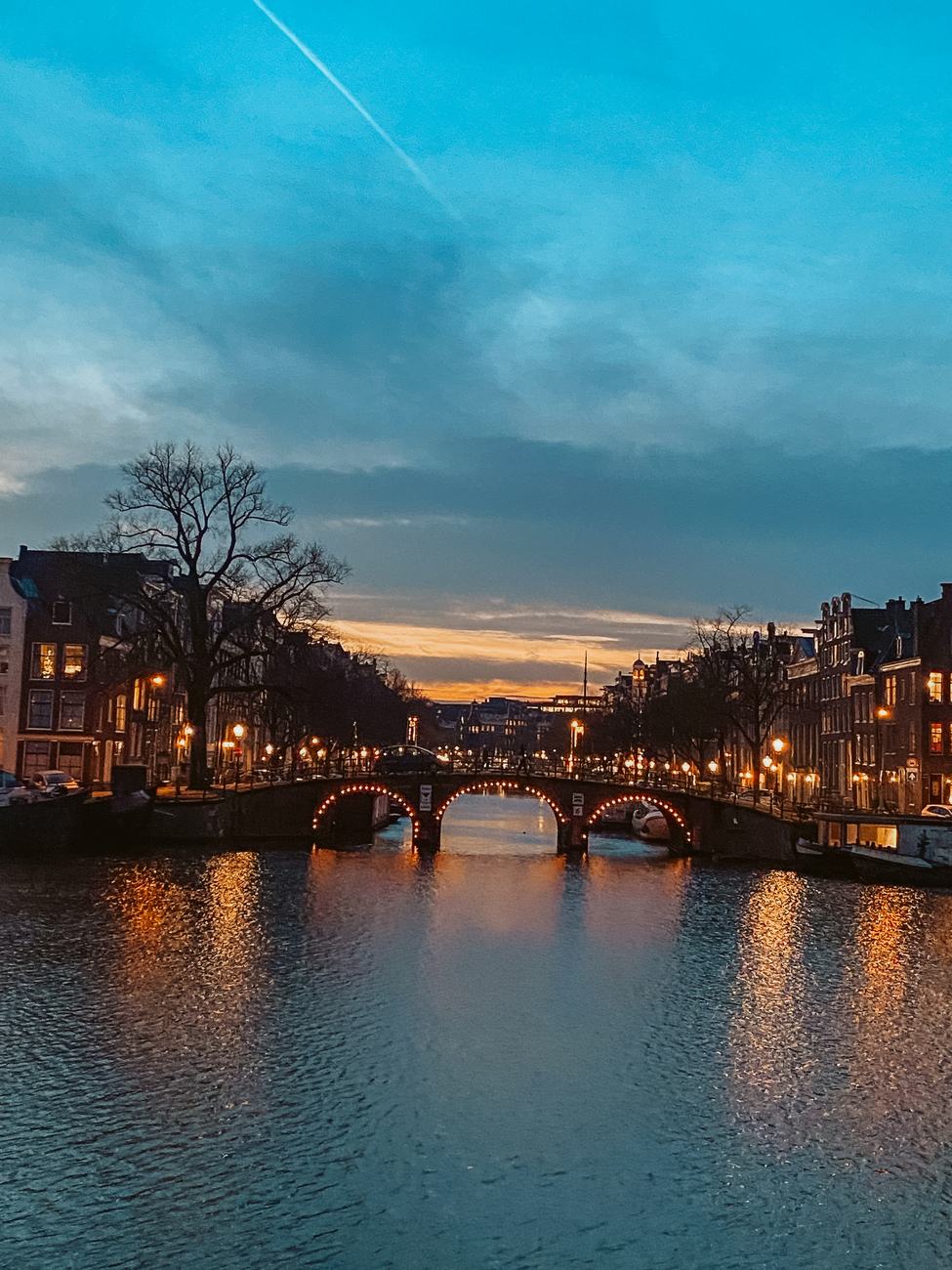 Amsterdamse gracht in de schemering, een verlichte brug weerspiegeld in het water